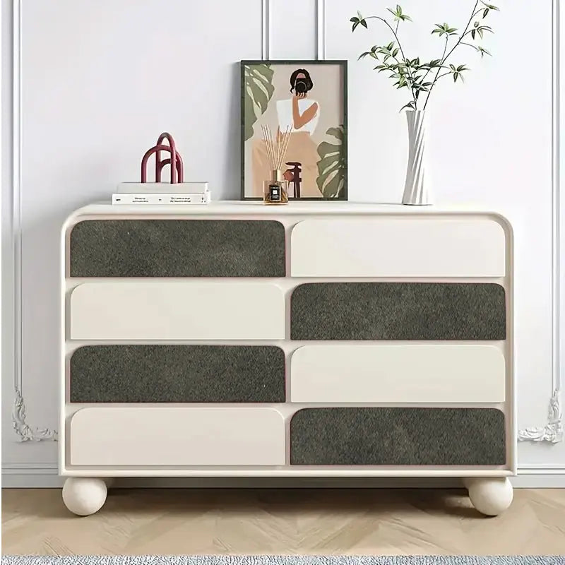 Cómoda blanca de cuatro cajones con tiradores de gamuza gris y detalles de madera clara.