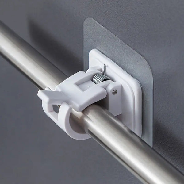 A white self-adhesive curtain rod clip hook is attached to a silver metal rod against a gray wall.
