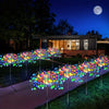 A row of colorful solar fireworks lights illuminating a lawn in the dark with a full moon visible.