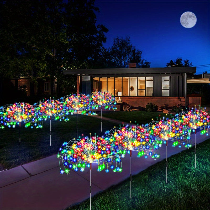 A row of colorful solar fireworks lights illuminating a lawn in the dark with a full moon visible.
